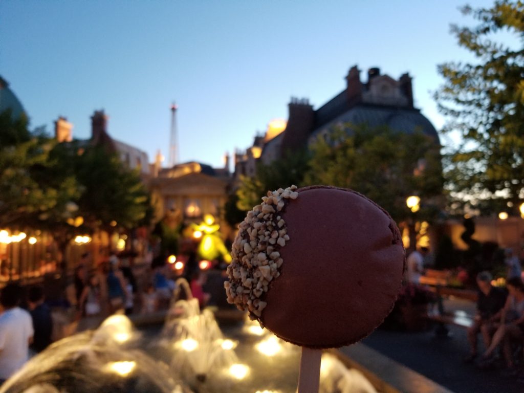 Macaron au Chocolat en Sucette—a Large Chocolate Macaron Lollipop in front of the fountain and Beauty and the Beast Topiary in the France Pavilion