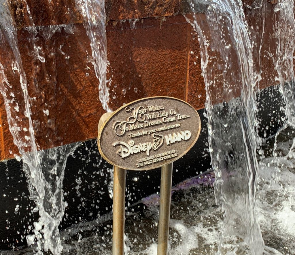 A sign in a fountain in Epcot for the Disney Hand program. 