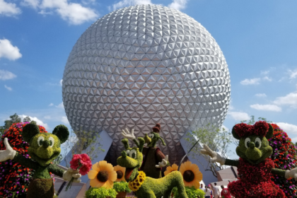 Picture of Spaceship Earth in Epcot with topiaries of Mickey Mouse, Minnie Mouse, Pluto and Goofy in the flowers in front of it on a sunny day with a few light clouds in the sky