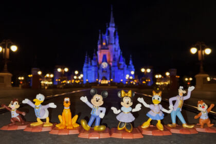 Picture looking into the hub in Magic Kingdom at Cinderella Castle with the "50" logo on it lit up at night and the Mcdonald's Happy Meal Toys of the Fab 8 Disney characters dressed in their 50th gear lined up on the ground in front of it.
