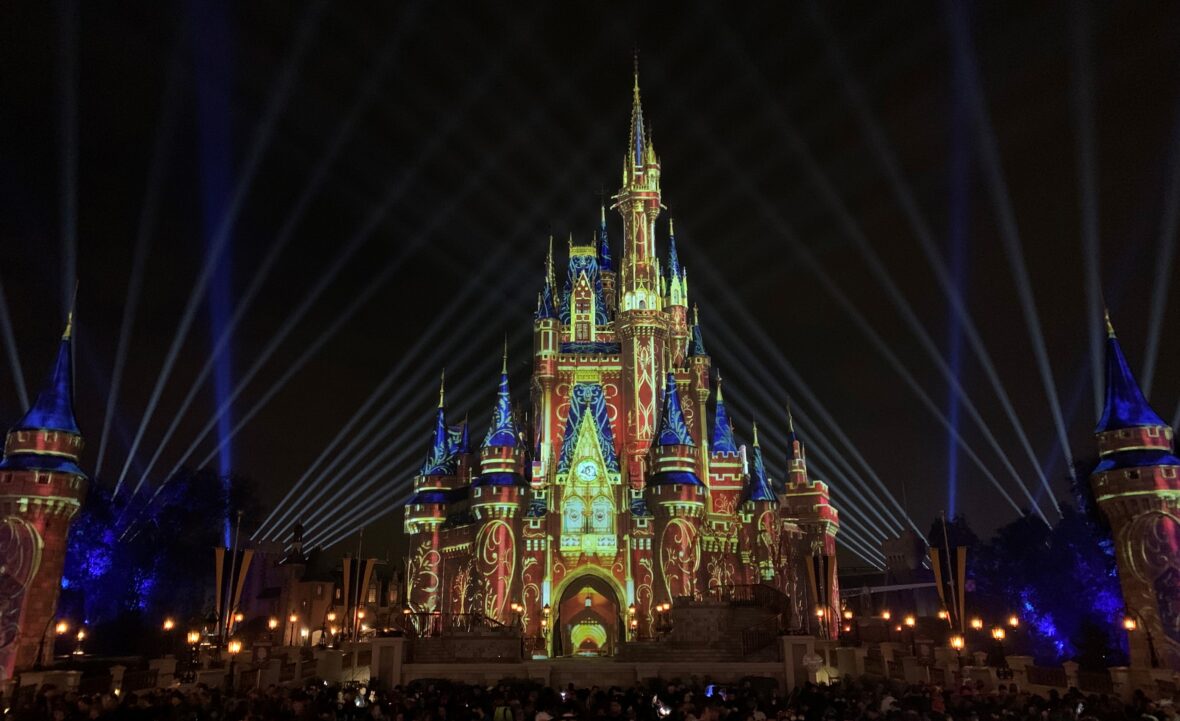 Cinderella Castle lit up at the end of "Happily Ever After" with red and yellow artistic lines with blue turrets in Magic Kingdom in Walt Disney World