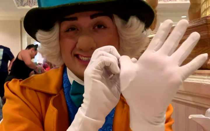 Picture of the Mad Hatter counting on his fingers in his top hat with a mustard yellow coat, a blue vest, and a teal bowtie at the Supercalifragilistic Breakfast held at 1900 Park Fare in Disney’s Grand Floridian Resort and Spa