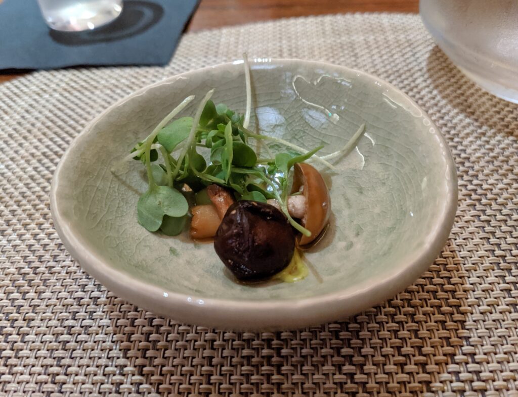 Picture of a small bowl with two small mushrooms over a yellow sauce topped with small greens