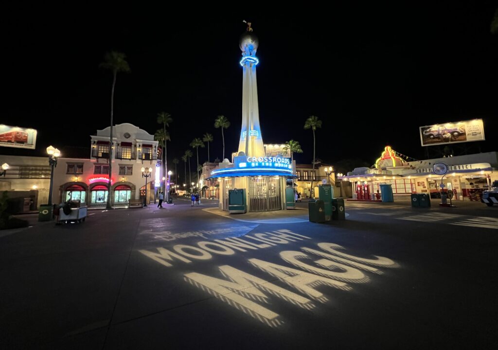 The "Disney Vacation Club Moonlight Magic" sign illuminated on the ground at Disney's Hollywood Studios in front of the Crossroads of the World store with Mickey Mouse on top of the Globe at Night. 
